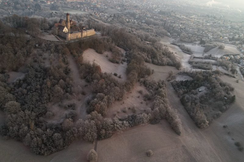Steiler Blick auf den bereiften Burgberg mit seinen Lichtungen und Wegen, die Burg oben links, Bamberg rechts im Tal. 22. Dezember 2021.