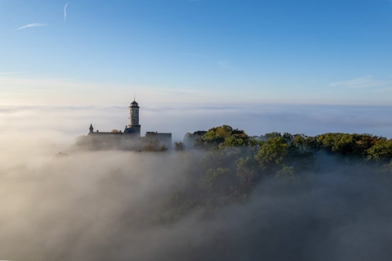 Die Burg tritt seitlich aus dem Morgennebel, darüber bereits klarer blauer Himmel. 30. September 2022.
