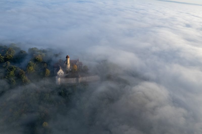 Blick von oben auf Ringmauer und runden Batterieturm, die Burg im aufsteigenden Nebel, ringsum erste Herbstfärbung. 30. September 2022.