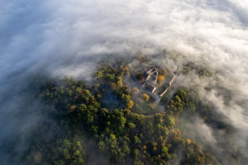 Senkrechter Blick auf Burg und bewaldete Bergkuppe im herbstlichen Hochnebel, erste Laubfärbung. 9. Oktober 2022.