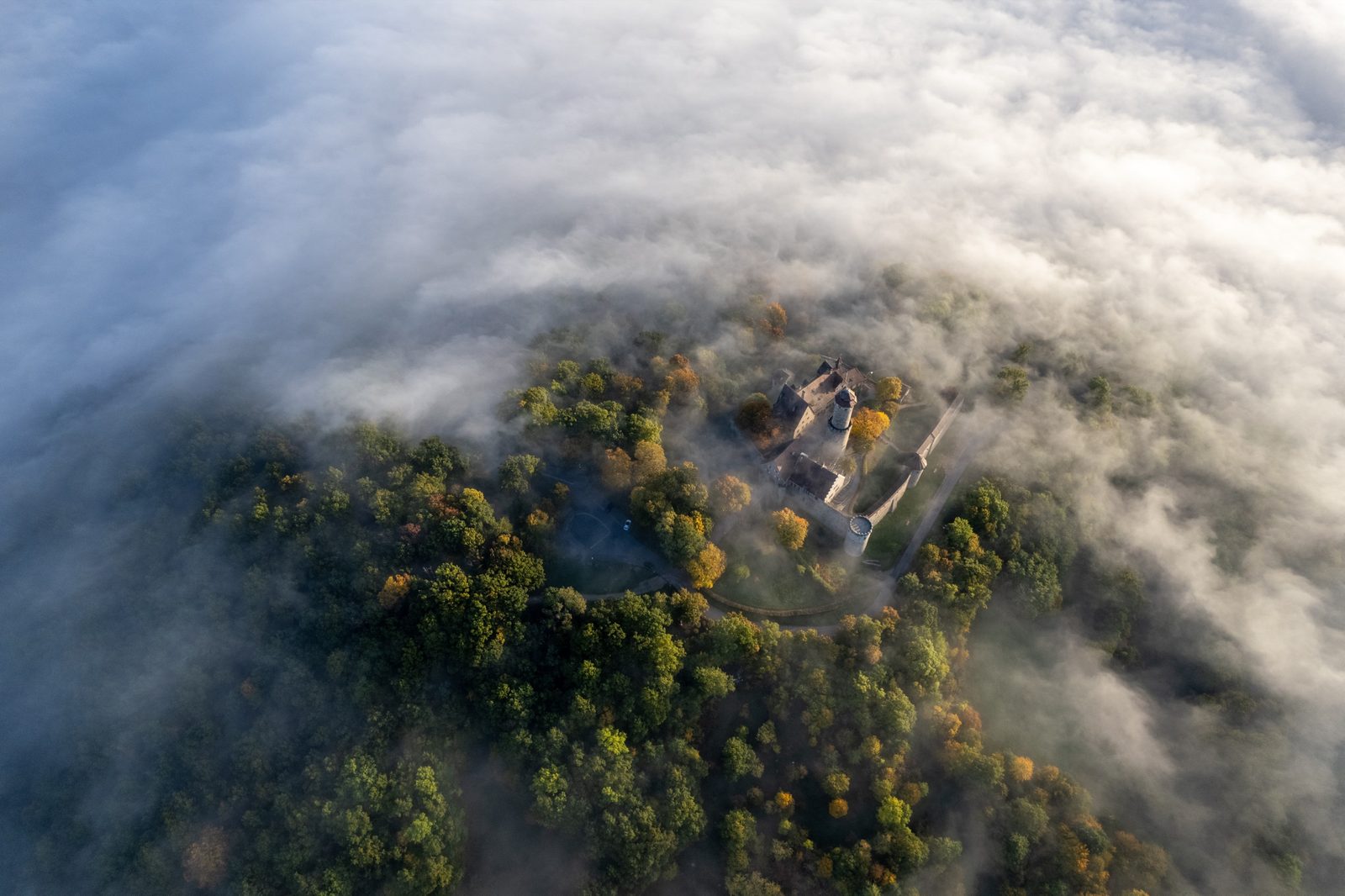 Senkrechte Luftaufnahme der Altenburg ob Bamberg auf ihrer herbstlich bewaldeten Bergkuppe, ringsum von Nebelschwaden umgeben